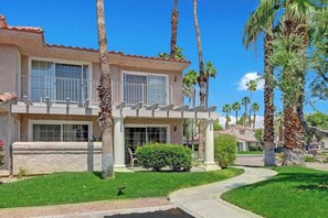 A two-story house with a balcony, surrounded by palm trees and a well-maintained lawn. - Mesquite Getaway - 2BR Condo with Pool and Views (Palm Springs)