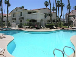 A swimming pool with lounge chairs and a building with balconies in the background. - Mesquite Getaway - 2BR Condo with Pool and Views (Palm Springs)