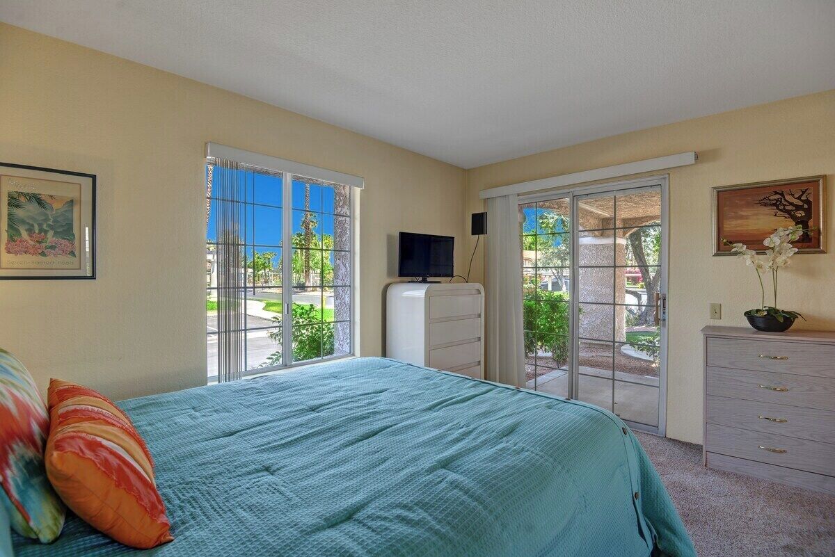 Un dormitorio con cama, televisor, cómoda y puerta corrediza de vidrio que da a un área exterior.