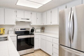 A modern kitchen with white cabinetry, a stainless steel refrigerator, a built-in oven, and a microwave. - Casa Palm Canyon - South PS (Palm Springs)