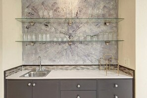 Eine Küche mit einer Glasablage, die Gläser beherbergt, einem Spülbecken und einer gefliesten Spritzschutzwand.