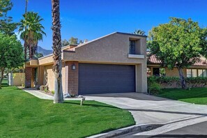 A modern two-story house with a garage, surrounded by well-maintained grass and palm trees. - Palm Springs Waterfront Oasis (Palm Springs)