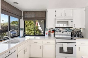 A modern kitchen with white cabinetry, a stainless steel sink, a built-in oven, and a microwave. - Sunrise Racquet Club Villa (Palm Springs)