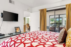 A modern hotel room with a large bed, a flat-screen TV mounted on the wall, and a sliding glass door leading to an outdoor area. - Sunrise Racquet Club Villa (Palm Springs)