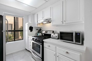 A kitchen with white cabinets, a stove, oven, microwave, and a window. - Canyon Country Club Chic (Palm Springs)