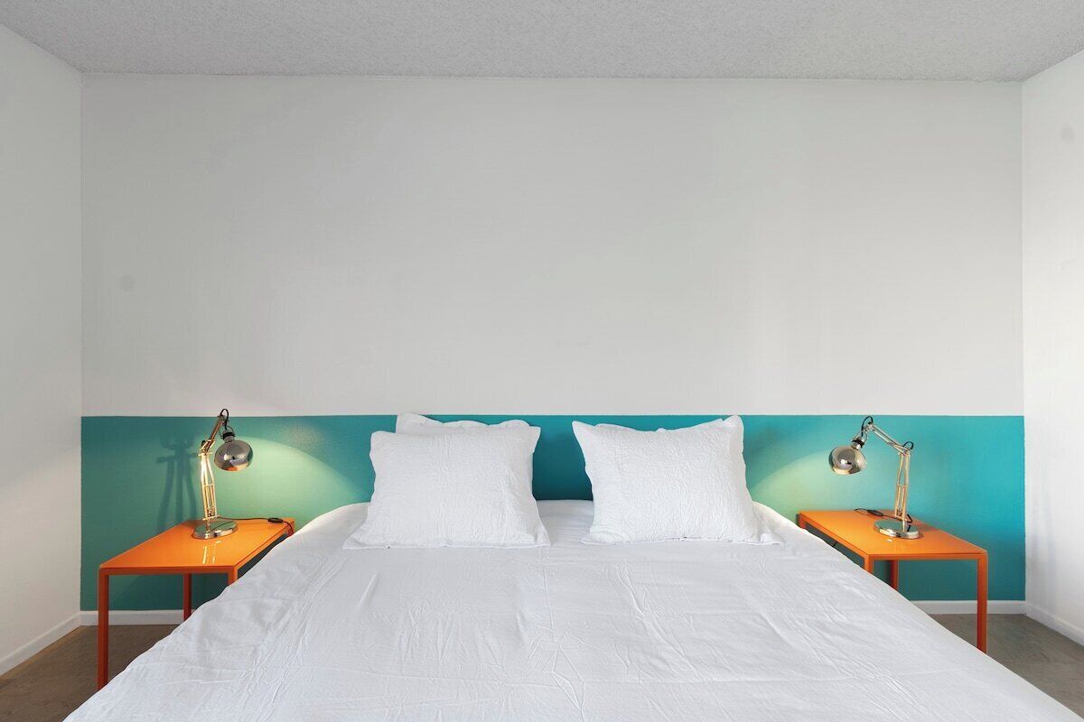 Una cama con ropa blanca, dos mesitas de noche con lámparas y una pared de acento color turquesa.