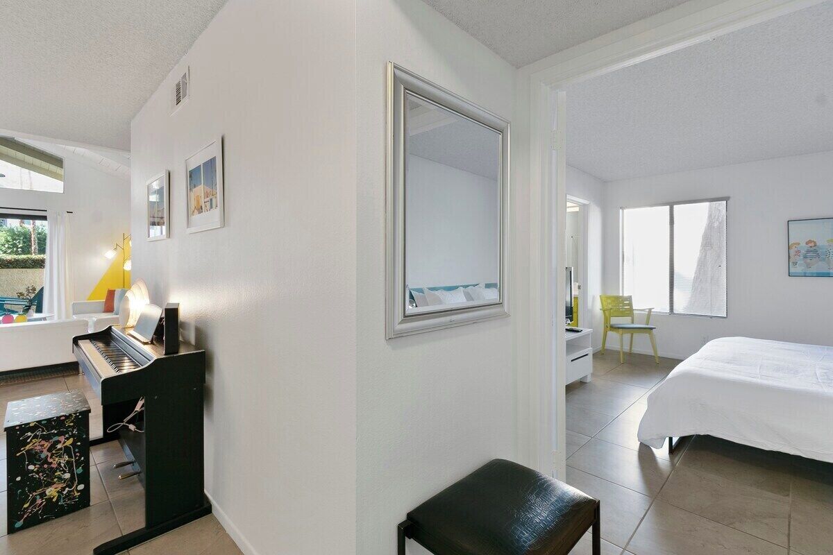 Ett hotellrum med ett piano, en säng, en stol och en stor spegel.