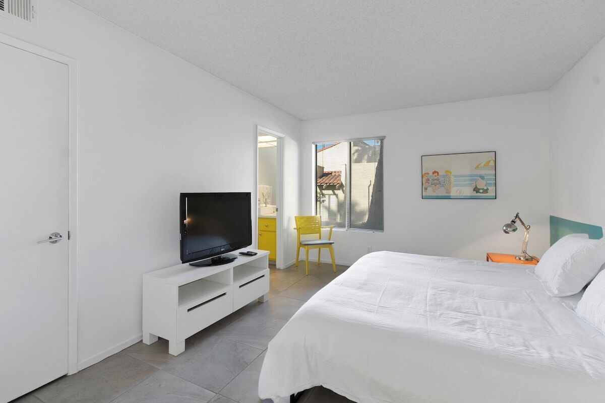 A bedroom with a bed, a TV on a stand, a chair, and a painting on the wall.