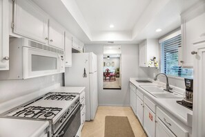 Une cuisine compacte avec des meubles blancs, une cuisinière à gaz, un four à micro-ondes et un réfrigérateur.