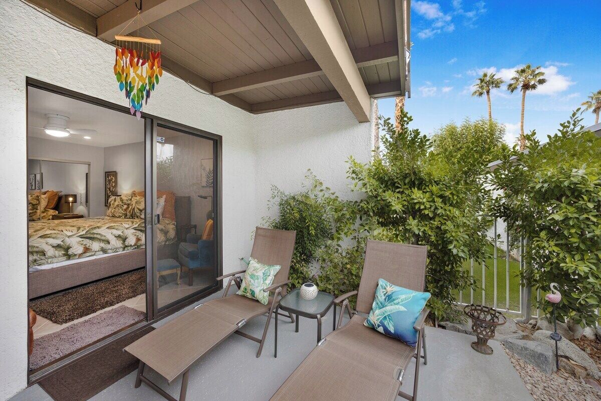 Un balcon aménagé avec un lit, deux chaises, une petite table et un carillon décoratif.