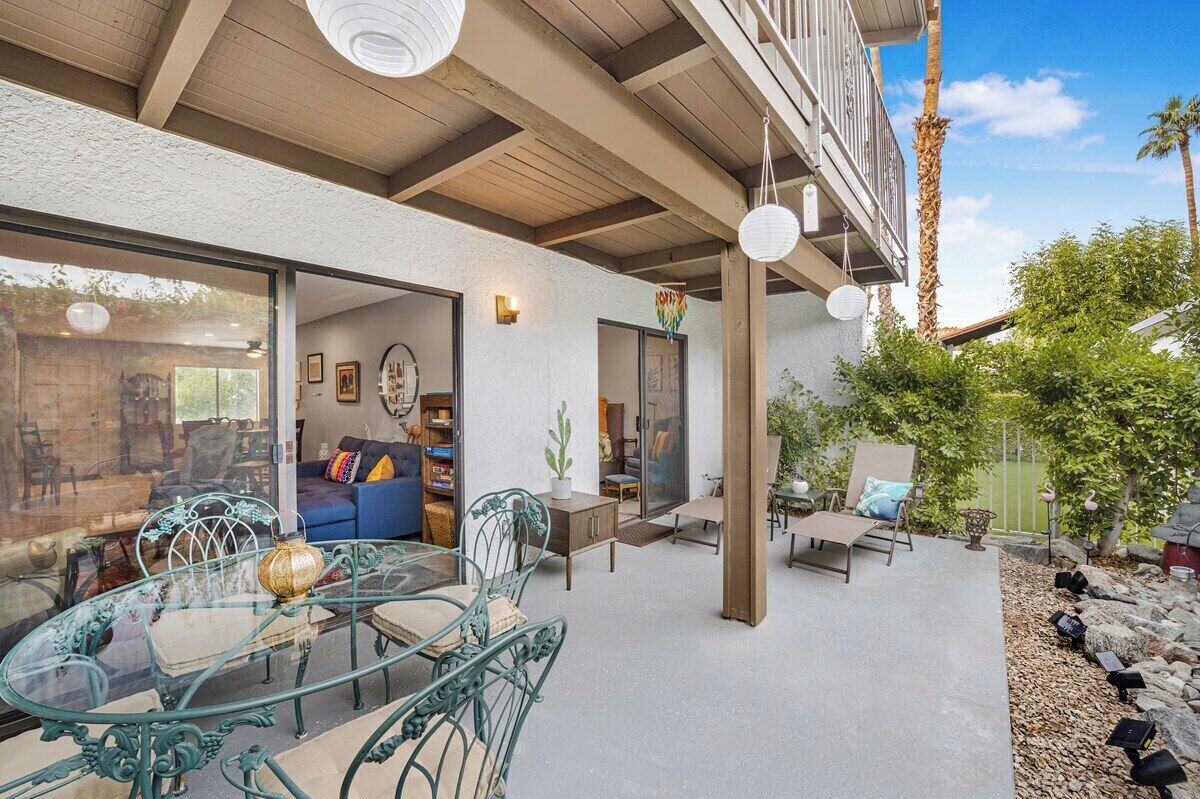 An outdoor patio with a glass table and chairs, a blue sofa, and a wooden deck.