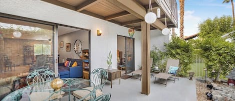 An outdoor patio with a glass table and chairs, a blue sofa, and a wooden deck.