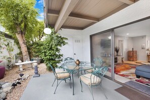 A patio with a glass table and chairs, surrounded by a garden with a tree and plants. - Estados Sanctuary - South Palm Springs (Palm Springs)
