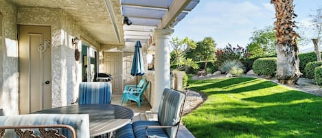 Eine Außenpatio mit Tisch und Stühlen, einer Pergola und einem gepflegten Rasen.