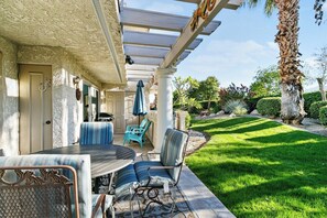 An outdoor patio with a table and chairs, a pergola, and a well-maintained lawn. - Mesquite Delight - 2BR Condo with Mountain Views (Palm Springs)