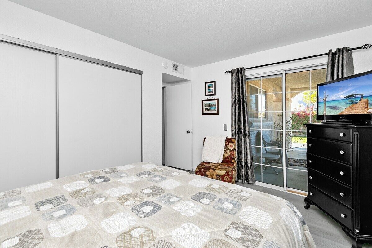 A bedroom with a bed, a television, a dresser, and a sliding glass door leading to a balcony.