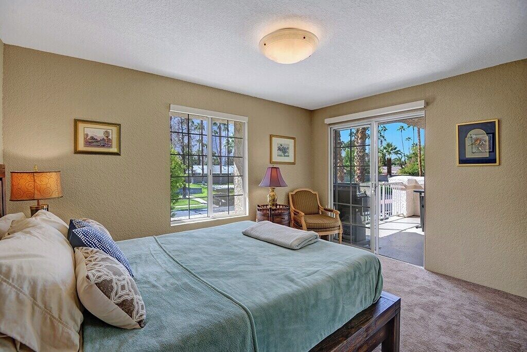 Une chambre à coucher comprenant un lit, une chaise, une lampe et une vue sur l’extérieur grâce à une porte-fenêtre coulissante.