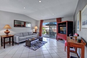 A modern living room with a sofa, coffee table, and TV stand, a balcony with a glass door, and a dining area with a table and chairs. - The Mesquite Mesmeric (Palm Springs)