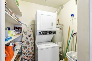 A compact laundry room with a front-loading washer and dryer, shelves with cleaning supplies, and a mop leaning against the wall. - La Palme Urban Chic Palm Springs Condo (Palm Springs)