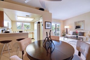 A modern living room with a round dining table, a sofa, and a kitchen area with a refrigerator and cabinets. - Mesquite Comfort Phase 2 (Palm Springs)