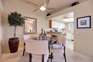 A dining area with a round table, four chairs, a ceiling fan, a large mirror, and a potted plant. - Mesquite Comfort Phase 2 (Palm Springs)