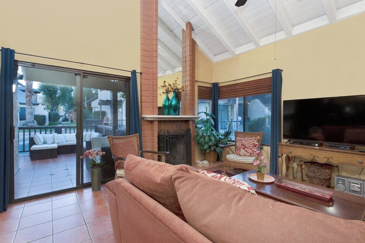 A living room with a fireplace, a sofa, a television, and a sliding glass door leading to an outdoor area.