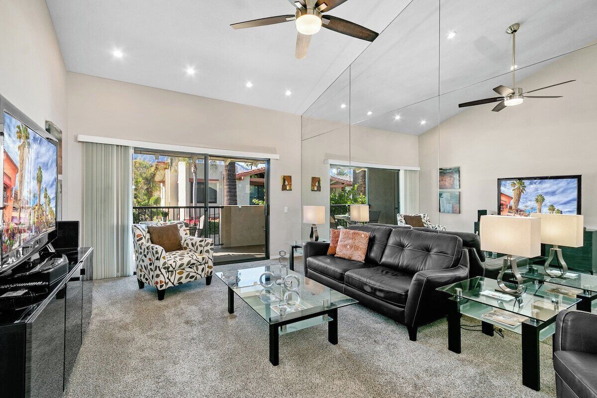 A spacious living room with a glass coffee table, a leather sofa, a patterned armchair, and a piano.