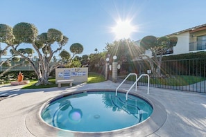 Piscina sob um céu ensolarado, cercada por árvores e um muro.