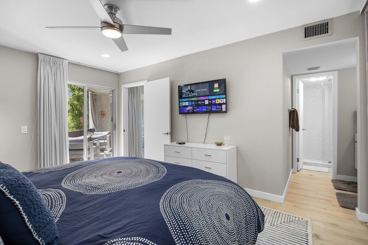 Une chambre à coucher avec un lit, un téléviseur fixé au mur et un ventilateur de plafond.