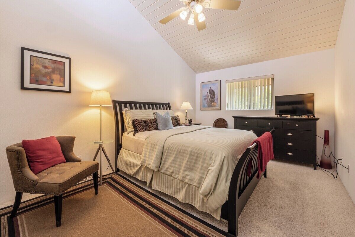 A bedroom with a bed, a chair, a lamp, a television, and artwork on the walls.