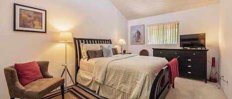 A bedroom with a bed, a chair, a lamp, a television, and artwork on the walls.