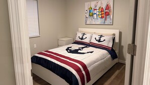 A bedroom with a bed, a nightstand, a wall-mounted painting, and a window with blinds. - 4 Bedroom Coastal Farmhouse In Cocoa Florida (Cocoa)