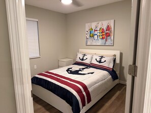 A bedroom with a bed, a nightstand, a wall-mounted painting, and a window with blinds. - 4 Bedroom Coastal Farmhouse In Cocoa Florida (Cocoa)