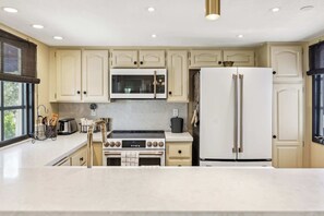A modern kitchen with white cabinetry, a stainless steel range, a microwave, a double-door refrigerator, and a gas stove. - Deauville Amora - Downtown PS (Palm Springs)