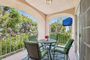 Un espace extérieur aménagé, couvert et doté de tables et de chaises, entouré d’une rambarde et offrant une vue sur un jardin avec des arbres et une marquise bleue.
