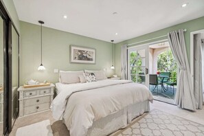 Une chambre avec un grand lit, des tables de chevet, une commode, un tableau encadré et une vue sur une terrasse extérieure.