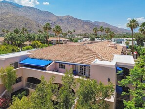Un hôtel dont le toit est recouvert de tuiles en terre cuite, entouré de palmiers et avec des montagnes en arrière-plan.