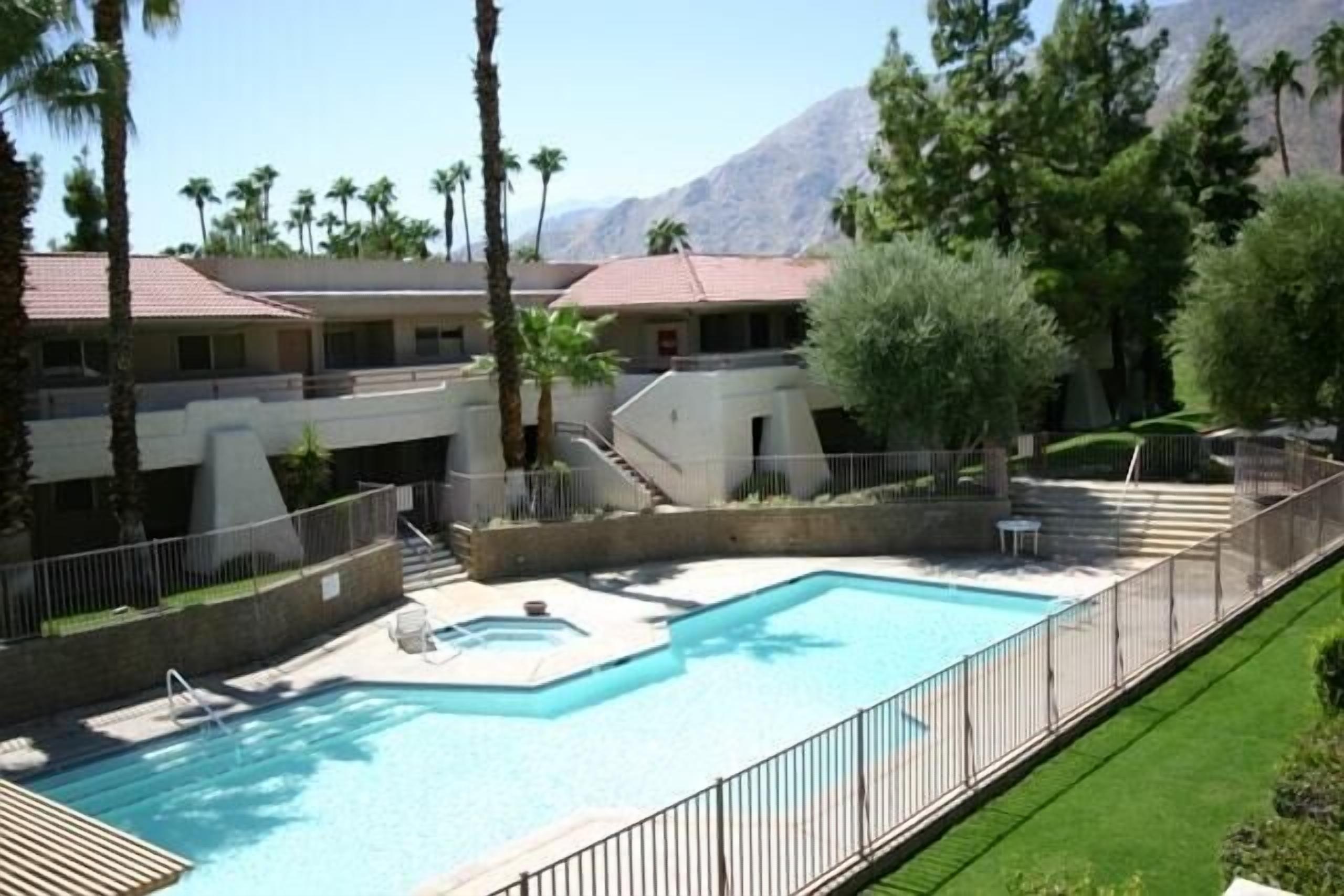 A swimming pool with a surrounding deck, palm trees, and a mountain in the background.