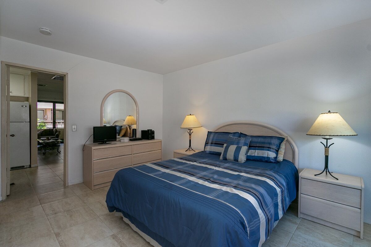 A bedroom with a bed, bedside tables, a dresser, a mirror, and a television.