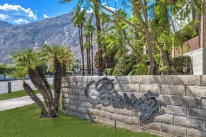 Eine Steinmauer mit der Schriftzug 'Barrington' in kursiver Schrift, umgeben von Palmen und mit Blick auf ein Gebirge.