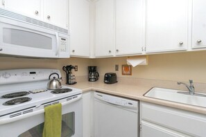 A compact kitchen with a microwave, stove, coffee maker, toaster, and dishwasher. - Biarritz Bliss (Palm Springs)
