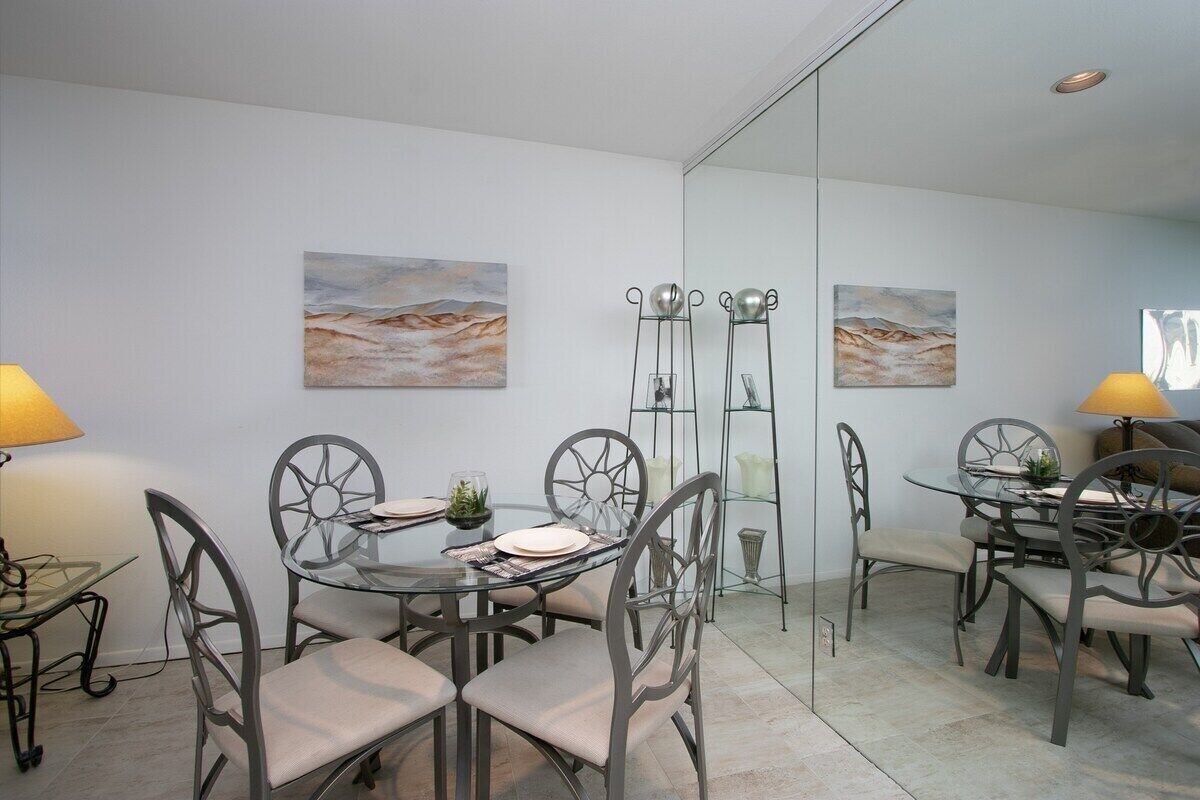 Un coin repas avec une table en verre et des chaises en métal, deux tableaux accrochés au mur et une cloison en verre.