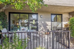 A patio with a glass table and chairs, a metal fence, and a building with a number '9' on the wall. - Midtown Mountain View Villa (Palm Springs)