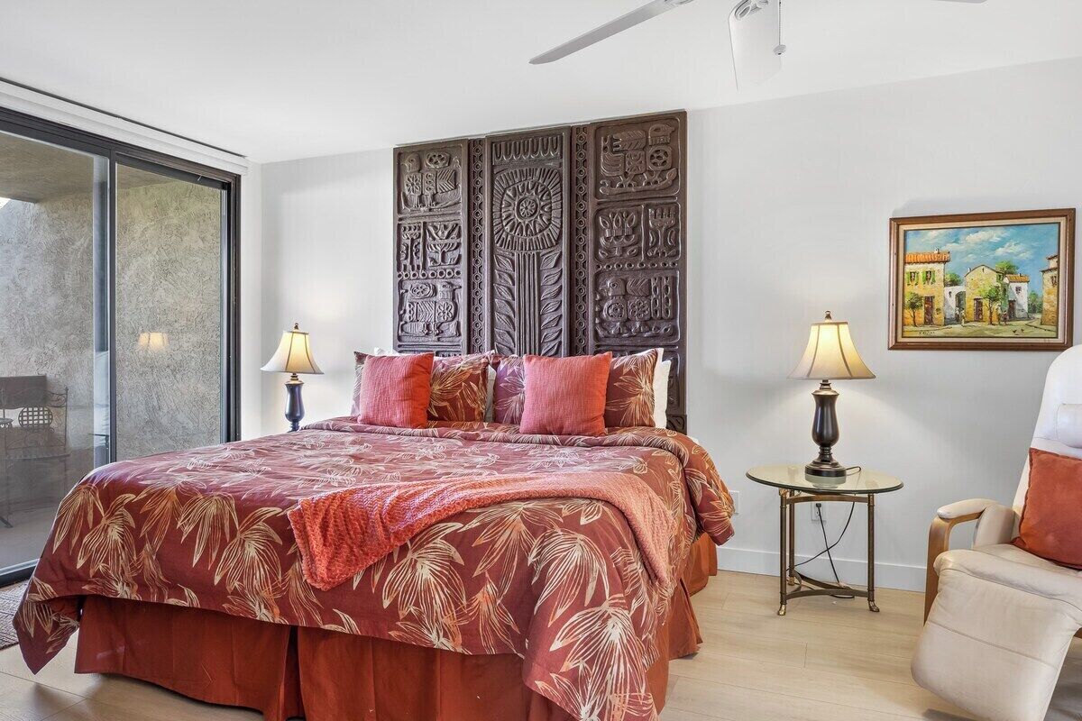 Een slaapkamer met een groot bed, een nachtkastje, een stoel, een schilderij en een decoratief wandpaneel.