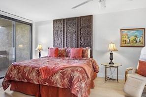 A bedroom with a large bed, a side table, a chair, a painting, and a decorative wall panel. - Midtown Mountain View Villa (Palm Springs)