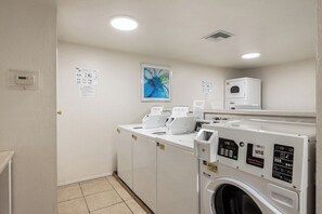A laundry room with a front-loading washer and dryer, a wall-mounted dryer, and a ceiling vent. - Ramon Estados Retreat (Palm Springs)