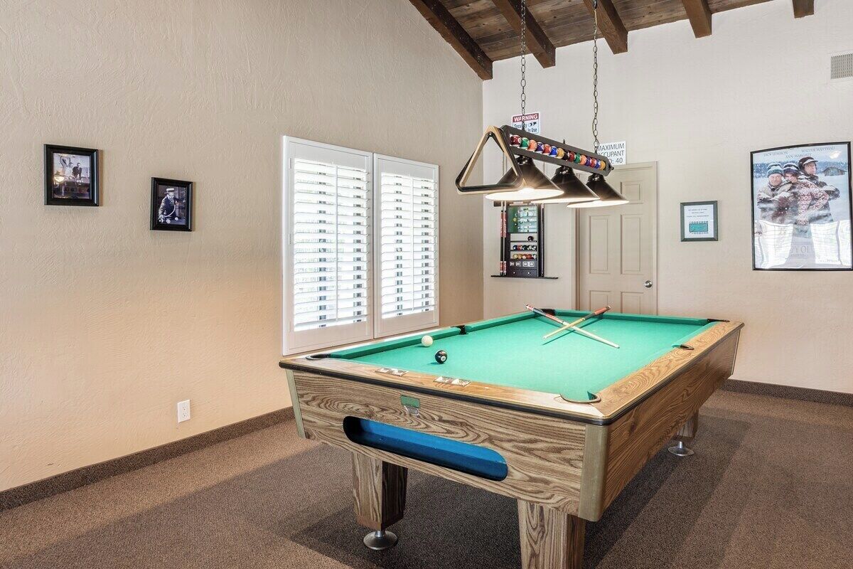 A pool table with a blue cushion, a hanging lamp, and framed pictures on the walls.