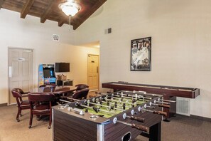 A room with a foosball table, a pool table, and a television. There are chairs and a door labeled 'Men.' - Ramon Estados Retreat (Palm Springs)