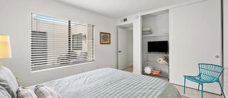 Un dormitorio con cama, una silla, un televisor y un armario.