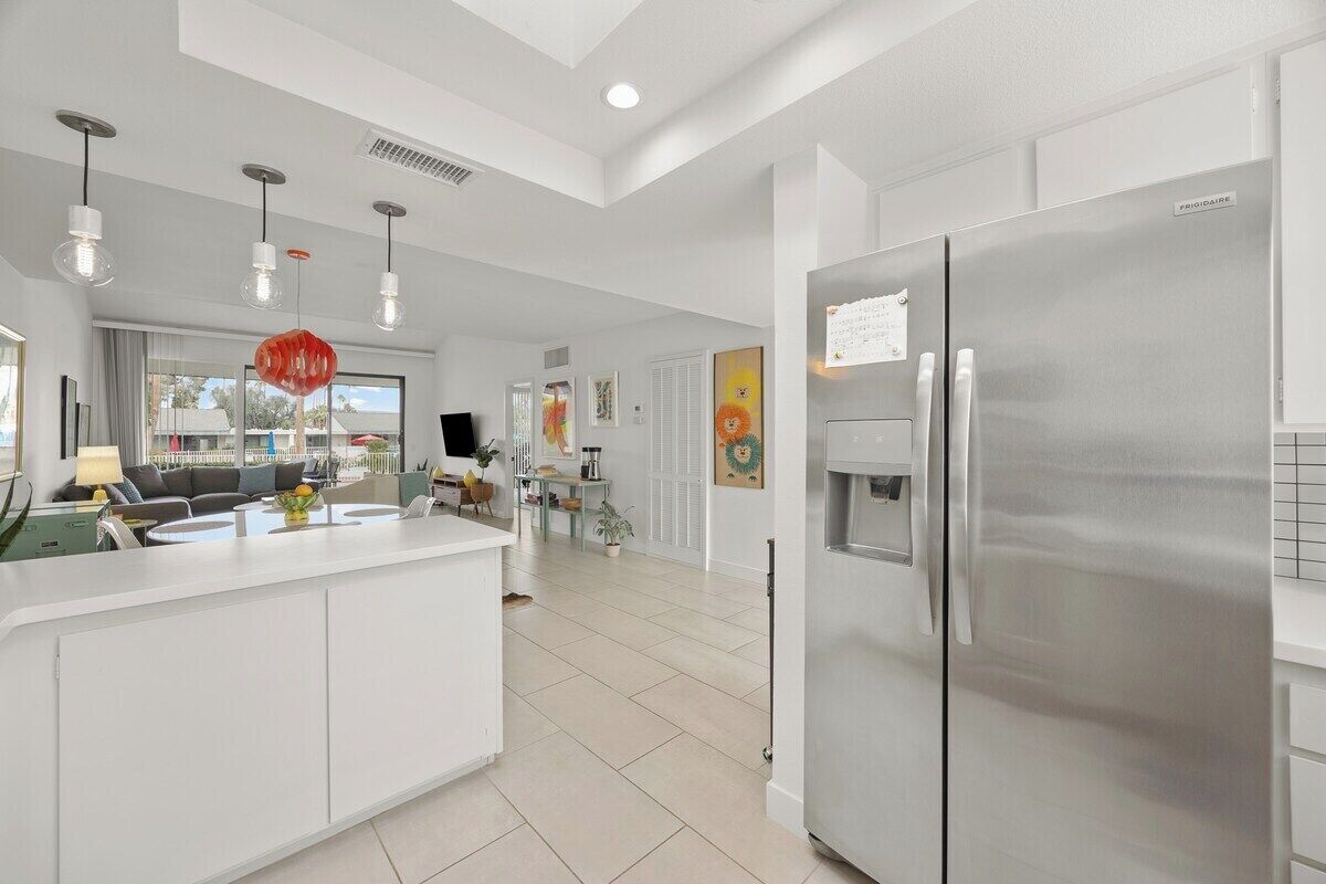 A modern kitchen with a stainless steel refrigerator, white cabinetry, and pendant lighting.